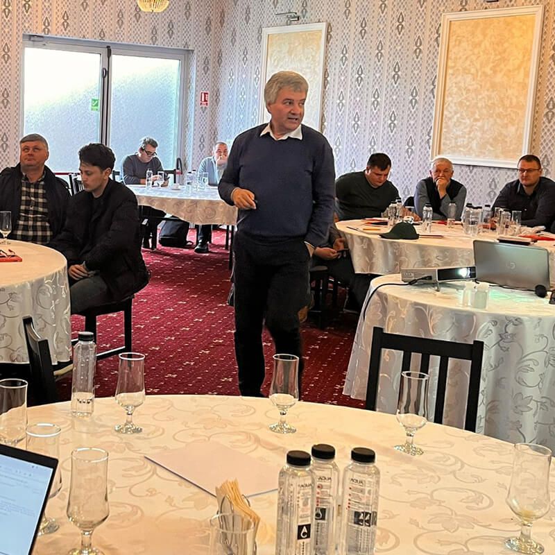 Formator UnivAgx vorbind participanților așezați la mese rotunde, într-o sală de curs.